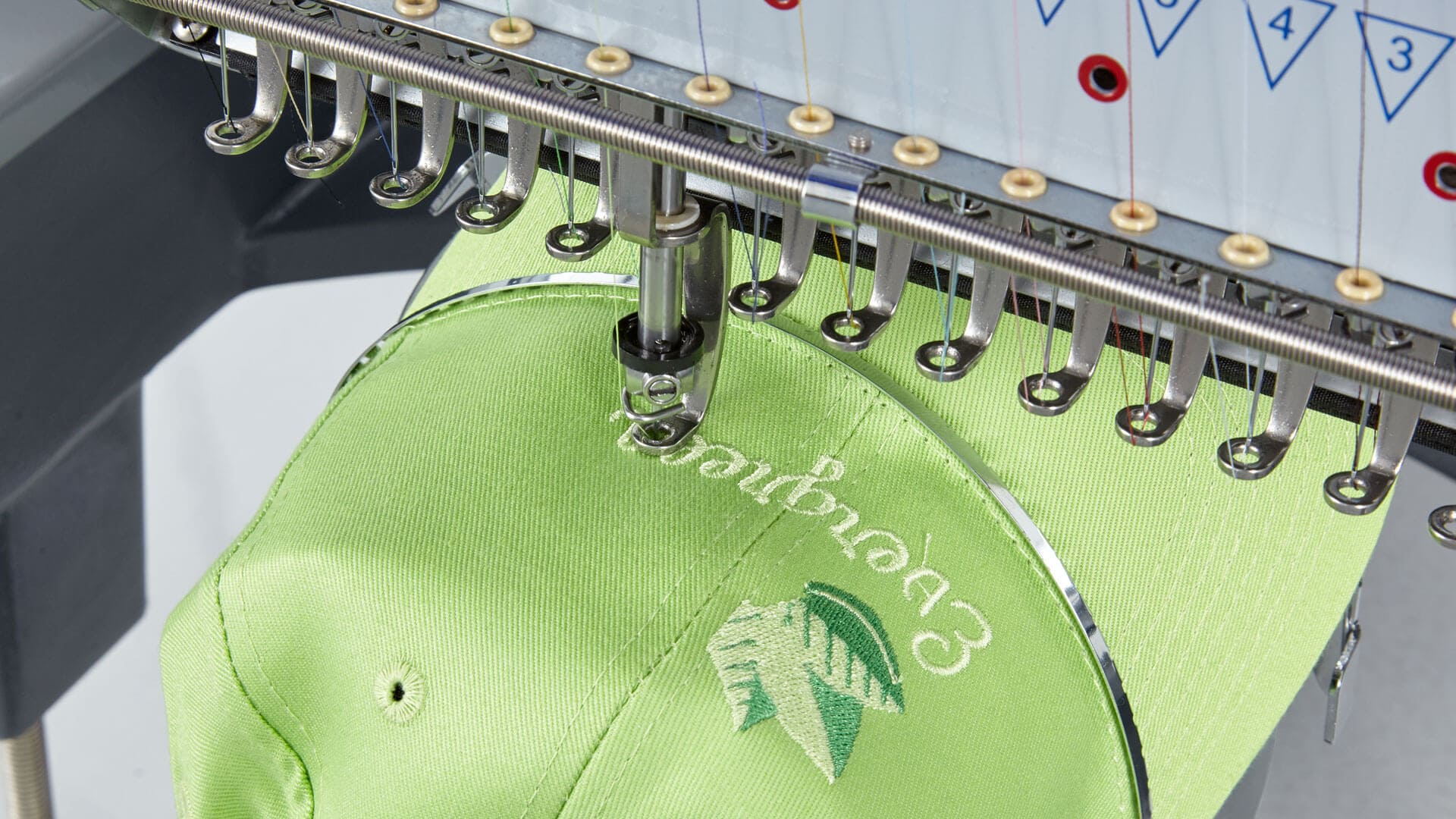 Hellgrüne Kappe mit Blatt-Logo im Stickvorgang auf einer Mehrkopf-Stickmaschine