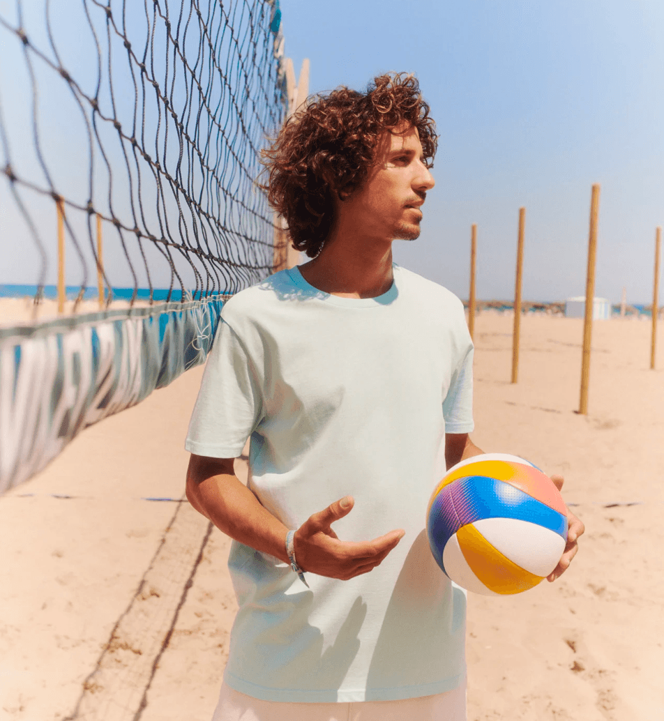 Offizielles Stanley/Stella-Lifestyle-Foto: eine Person am Strand in mintfarbenem T-Shirt mit einem Beachvolleyball